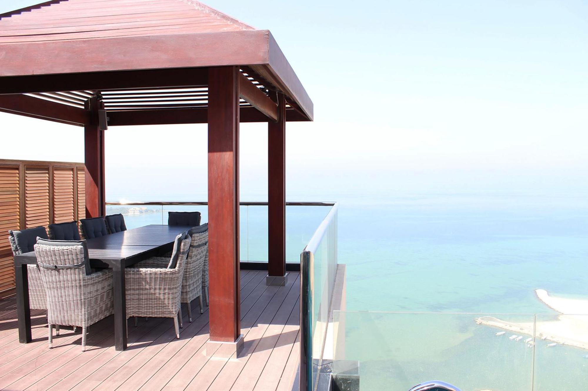 Lagoona Beach Luxury Resort And Spa Manama Dış mekan fotoğraf The photo showcases a stylish outdoor patio or terrace area. It features a wooden structure with a sloped roof, providing a shaded space. There is a large table made of dark wood, surrounded by several wicker chairs. The patio is elevated and has gla