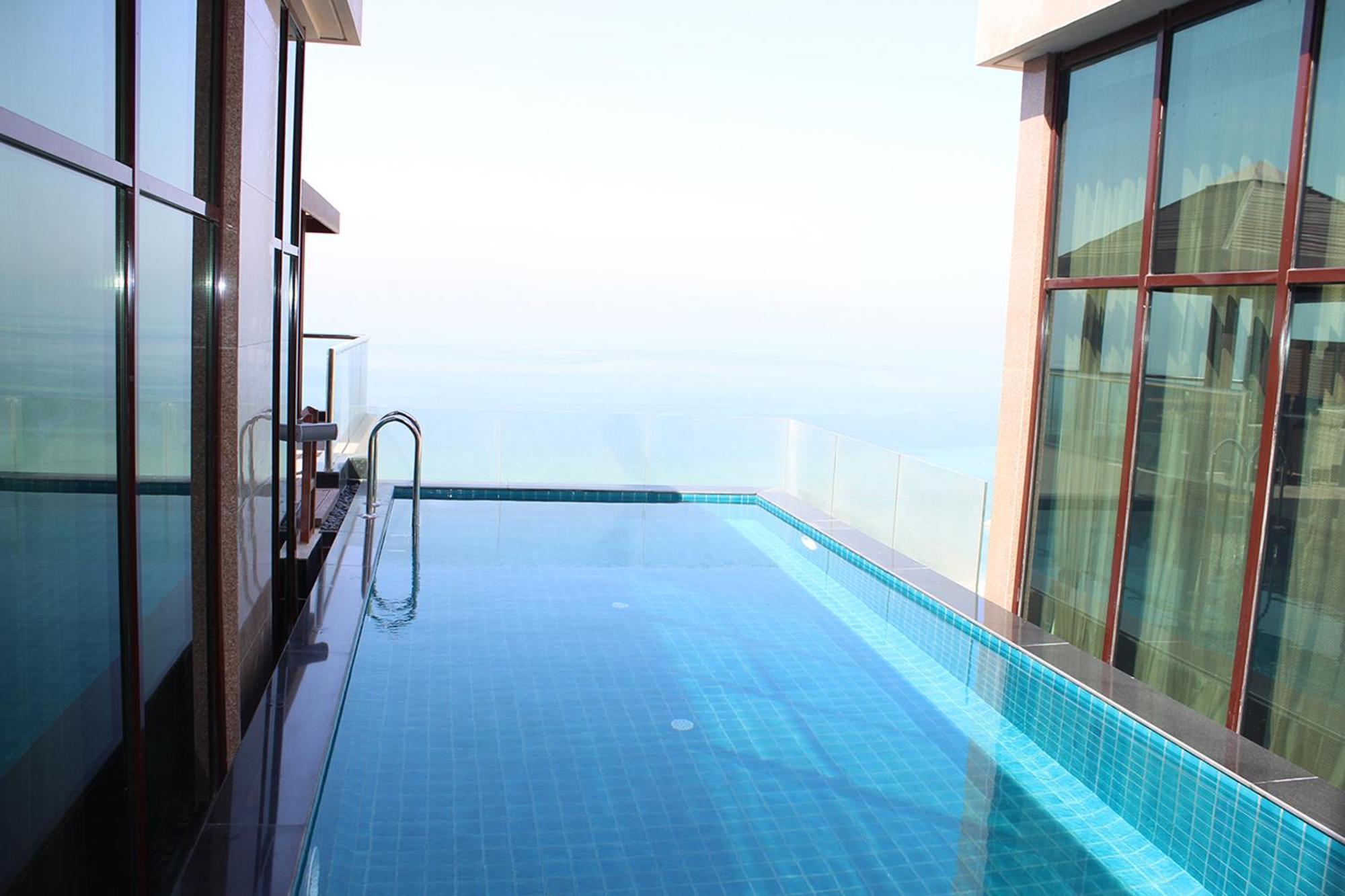 Lagoona Beach Luxury Resort And Spa Manama Dış mekan fotoğraf The photo shows an infinity pool situated on a balcony or rooftop, with a clear view extending to the horizon. The pool has a sleek design with blue tiles, and it appears to be reflecting the sky. There is a ladder on one side for access into the poo