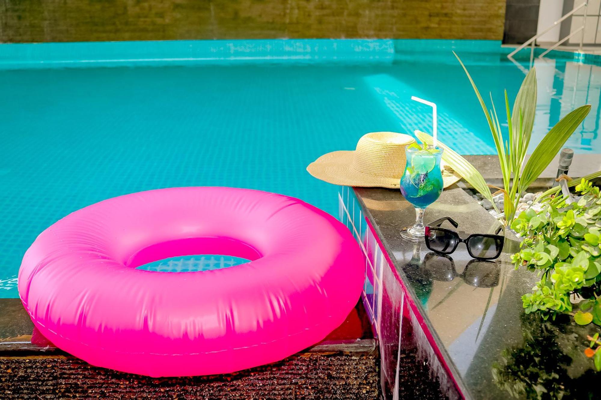 Lagoona Beach Luxury Resort And Spa Manama Dış mekan fotoğraf The photo shows a vibrant and inviting scene by a swimming pool. In the foreground, there is a large pink inflatable float and a stylish straw hat. Next to the float, a refreshing cocktail in a glass is displayed, complete with a straw and garnishes.