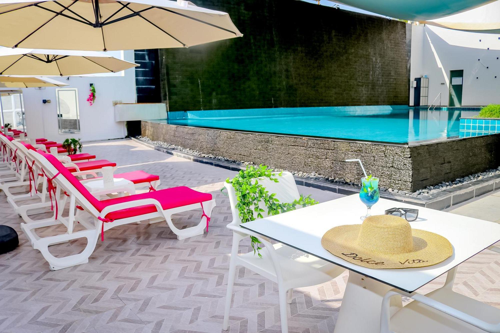 Lagoona Beach Luxury Resort And Spa Manama Dış mekan fotoğraf The photo shows a sunny poolside area with bright red lounge chairs arranged neatly beside a swimming pool. There are large beige umbrellas providing shade. A small table is set up with a straw hat and a colorful drink, suggesting a relaxed, tropical