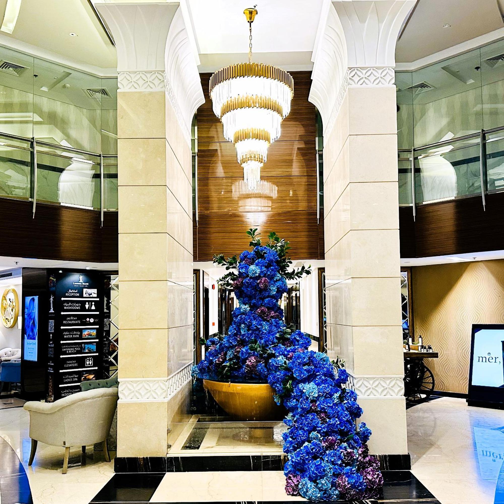 Lagoona Beach Luxury Resort And Spa Manama Dış mekan fotoğraf The photo depicts an elegant lobby or entrance area of a building. Central to the scene is a large floral arrangement featuring vibrant blue flowers. This arrangement is positioned in a decorative bowl. Above it hangs a stylish chandelier with a laye