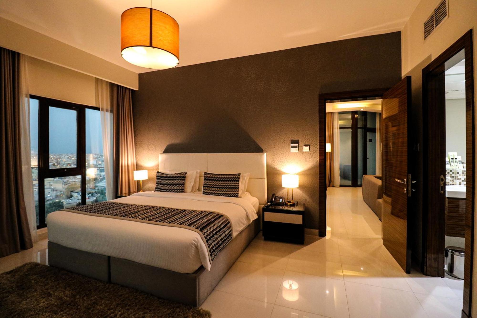 Lagoona Beach Luxury Resort And Spa Manama Dış mekan fotoğraf The photo depicts a modern hotel room or suite. It features a large bed with a white and gray color scheme, accented with decorative pillows. On either side of the bed, there are sleek bedside lamps providing warm lighting. The walls are a dark color