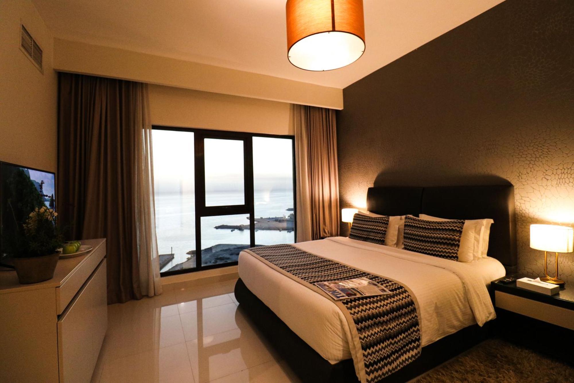 Lagoona Beach Luxury Resort And Spa Manama Dış mekan fotoğraf The photo shows a modern hotel room featuring a neatly made bed with decorative pillows. The room has a stylish design with a dark accent wall and a large window that offers a view of the outdoors. Natural light comes in, giving the space a bright an