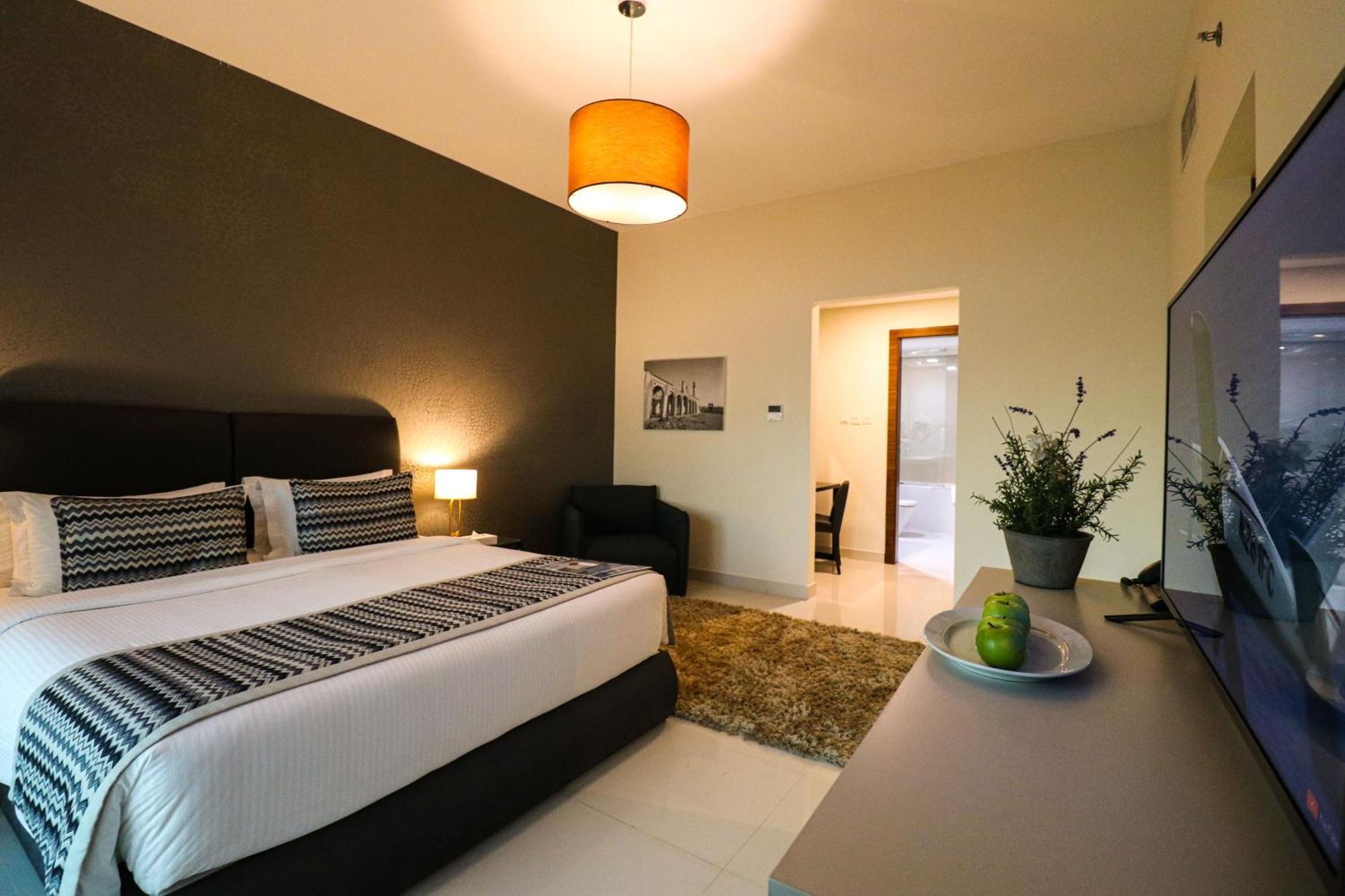 Lagoona Beach Luxury Resort And Spa Manama Dış mekan fotoğraf The photo shows a modern hotel room. It features a large bed with a neatly made white and dark-colored duvet. On either side of the bed, there are bedside tables with lamps. The wall behind the bed is painted in a dark color, creating a contrast with