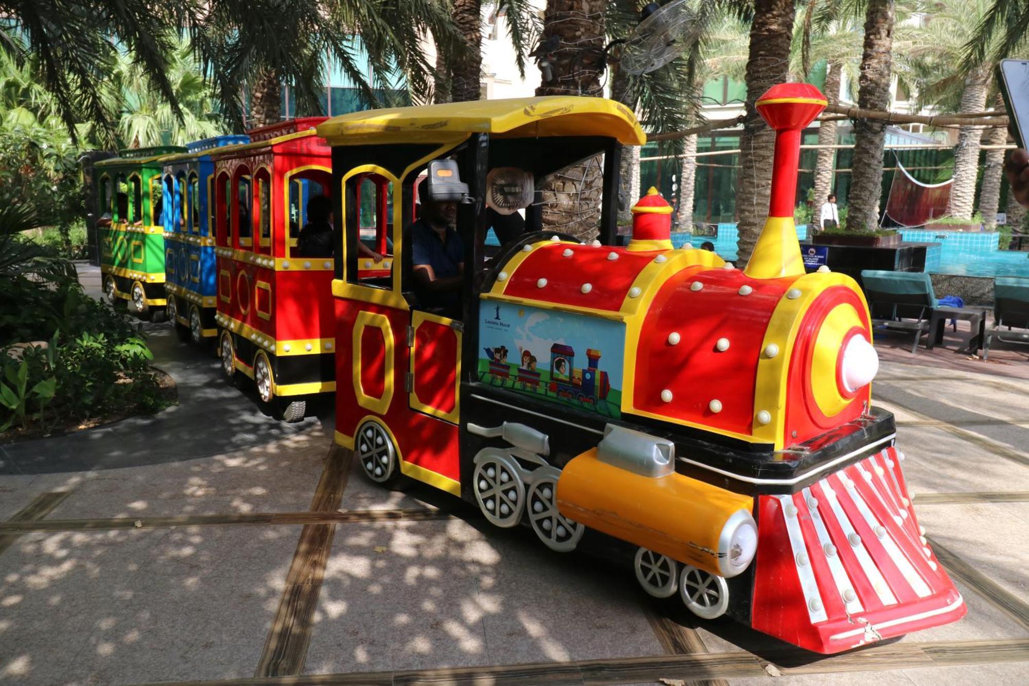 Lagoona Beach Luxury Resort And Spa Manama Dış mekan fotoğraf The photo shows a colorful miniature train. It features a vibrant design with bright red, yellow, and blue colors. The front of the train resembles a classic steam engine, complete with a prominent smokestack. The train is designed to resemble a fun 