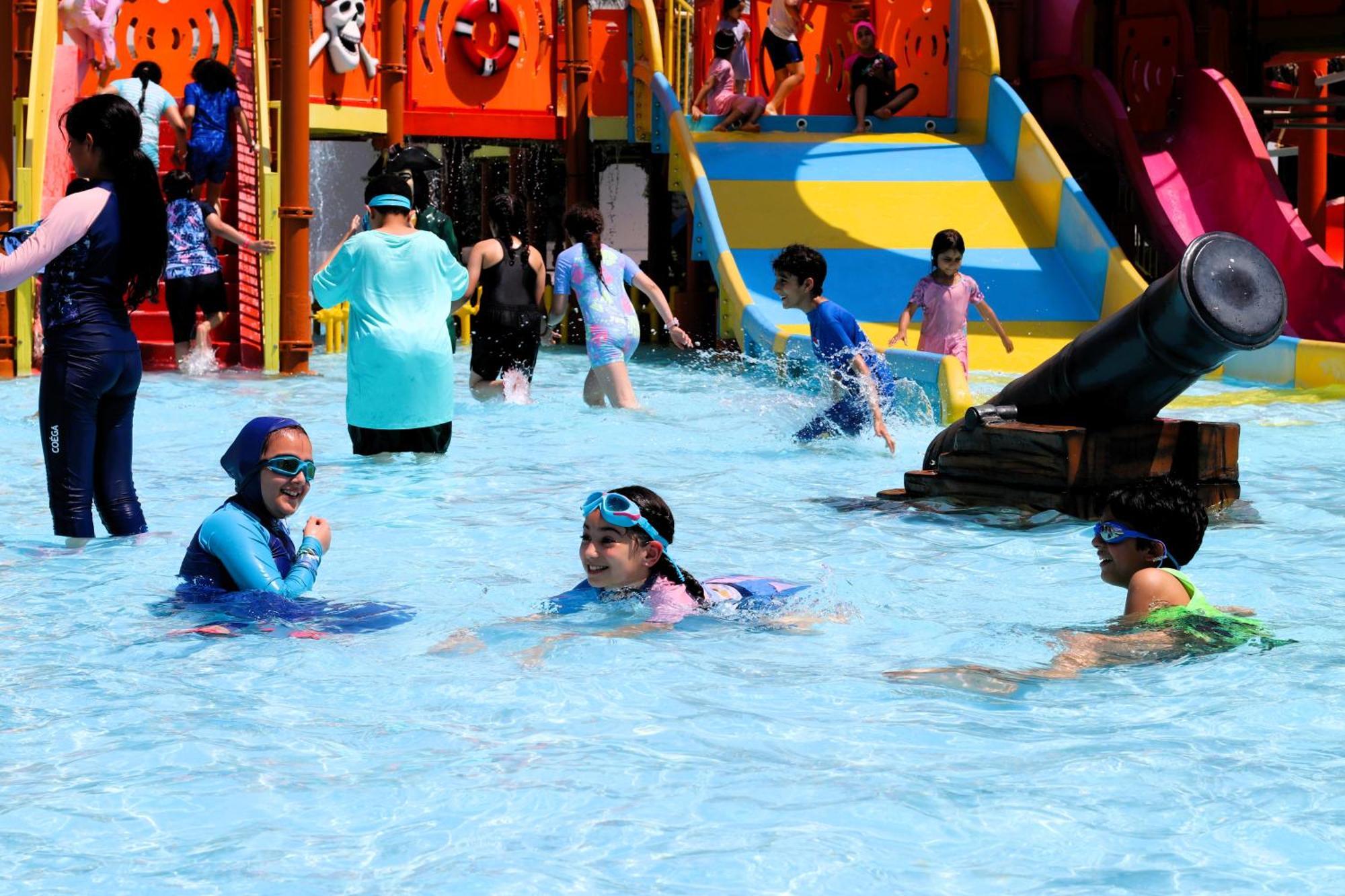 Lagoona Beach Luxury Resort And Spa Manama Dış mekan fotoğraf The photo shows a vibrant water park scene with several children playing in a shallow pool. Some are swimming and splashing around, while others are playing on colorful slides in the background. The atmosphere is lively and cheerful, with kids of var