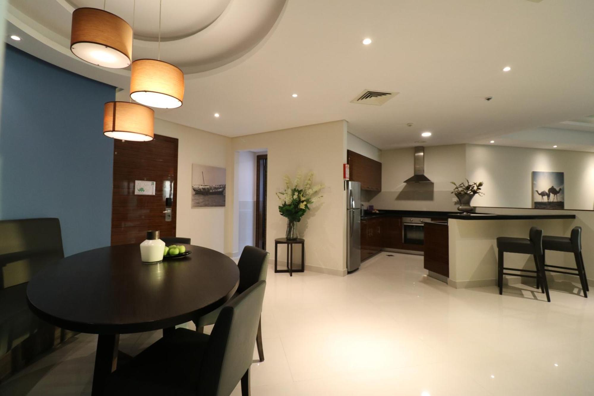 Lagoona Beach Luxury Resort And Spa Manama Dış mekan fotoğraf The photo shows a modern, open-concept dining and kitchen area. On the left, there is a round dining table with black chairs, accompanied by a few decorative elements like a small vase and some fruit. The walls have a combination of light and dark to