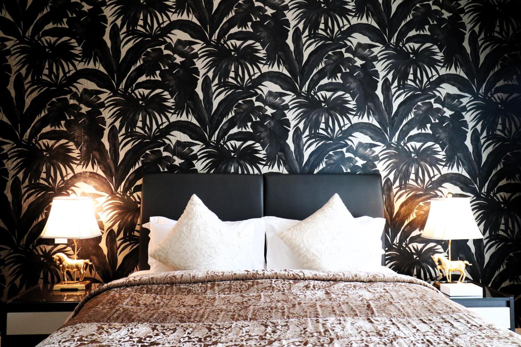 Lagoona Beach Luxury Resort And Spa Manama Dış mekan fotoğraf The photo depicts a stylish bedroom featuring a distinctive wall covered in a black and white tropical foliage wallpaper. The bed has a modern black headboard and is adorned with white pillows, creating a clean and elegant look. A textured brown thro