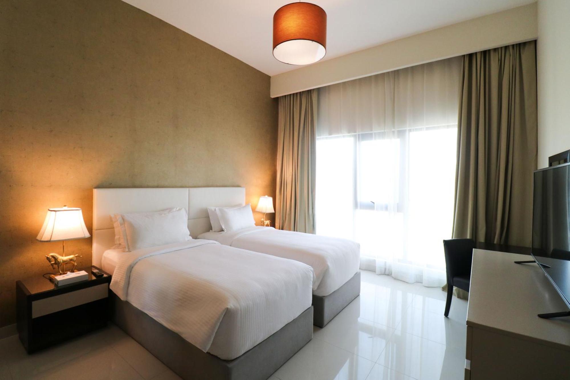 Lagoona Beach Luxury Resort And Spa Manama Dış mekan fotoğraf The photo shows a hotel room featuring two single beds with white bedding. The walls have a neutral tone, and there's a large window covered by light, sheer curtains allowing natural light to enter. On either side of the beds, there are bedside table