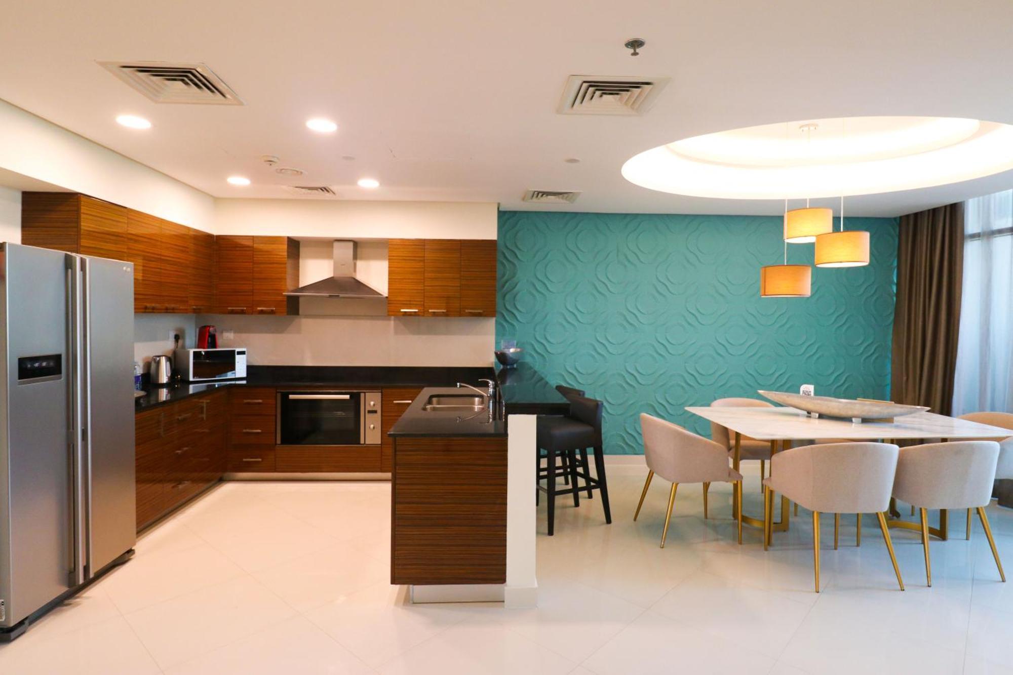 Lagoona Beach Luxury Resort And Spa Manama Dış mekan fotoğraf The photo shows a modern kitchen and dining area. The kitchen features wooden cabinets, sleek appliances including a stainless steel refrigerator, microwave, and an oven. There is a dark countertop and a small breakfast bar with high stools. The wall